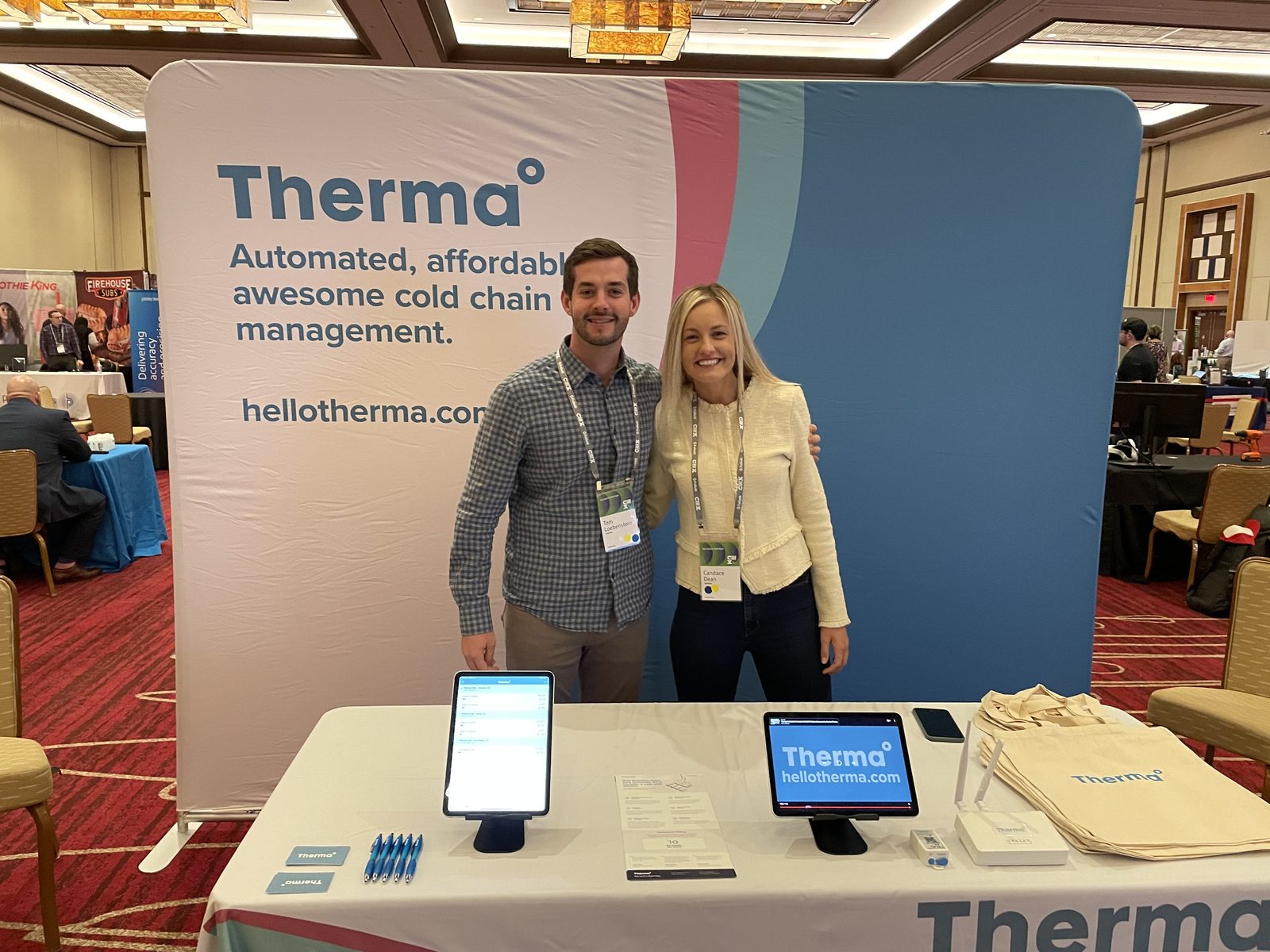 Tom Loebenstein and a colleague standing at the Therma trade show booth in a hotel ballroom.